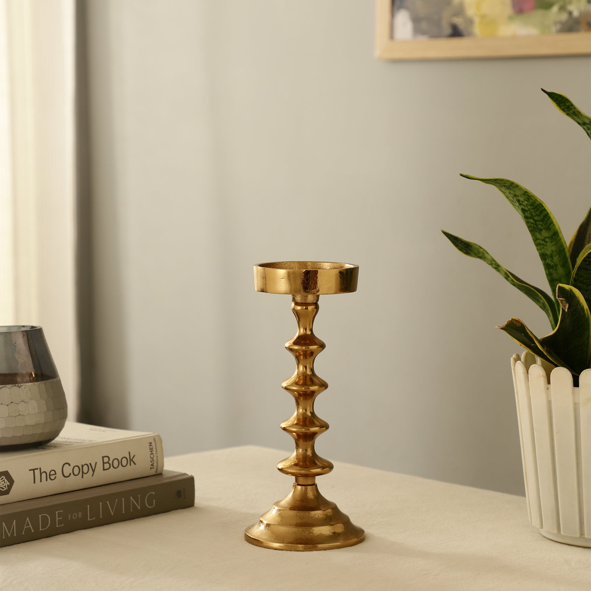 Gold candlestick on a surface with books and a plant in the background