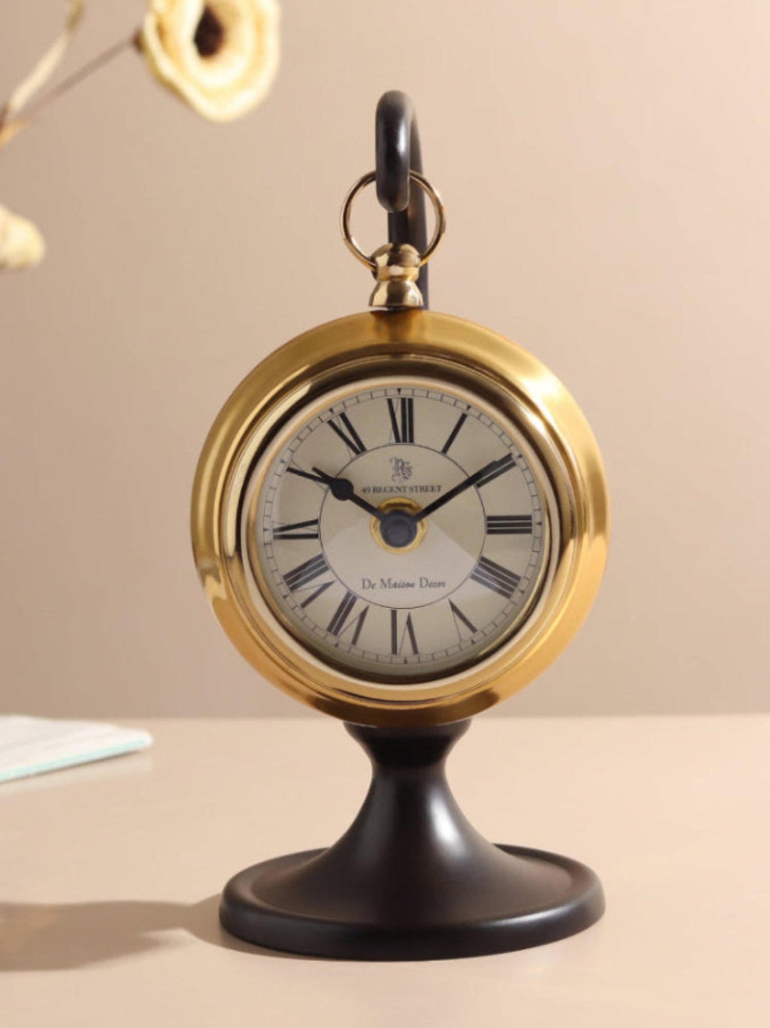 Decorative clock with gold frame and black base on a beige background