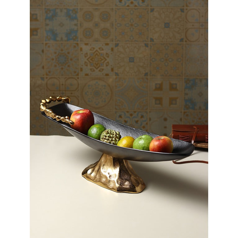 Decorative fruit bowl with gold base on a neutral surface with patterned wall in the background