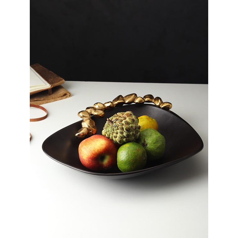 Black decorative bowl with gold accents containing fruits on a white surface.