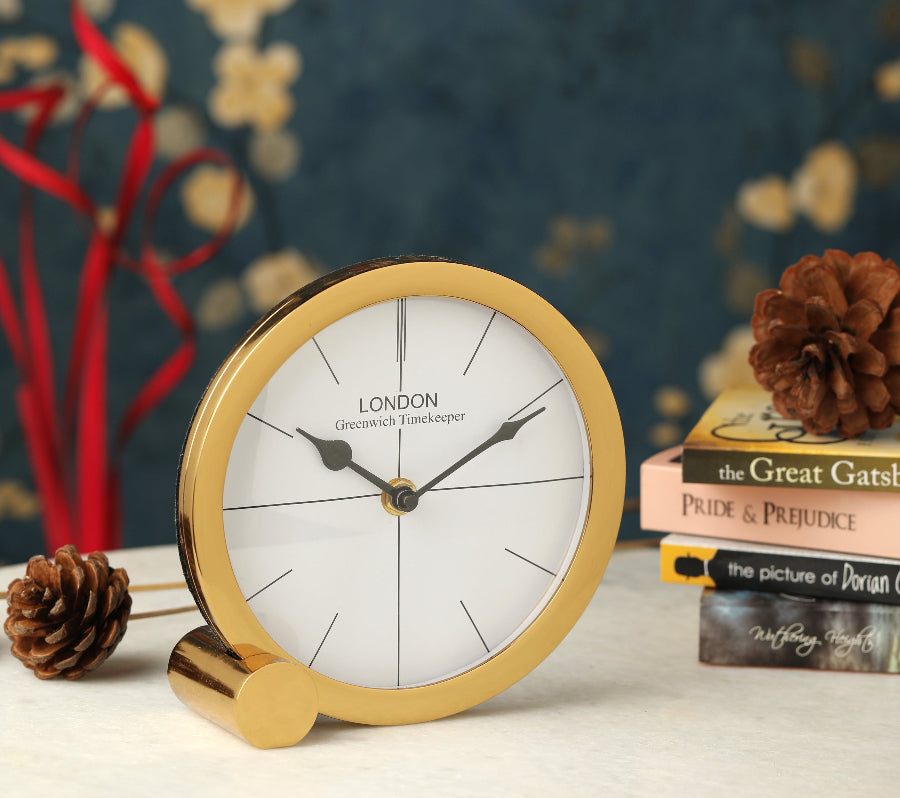 Gold-framed clock on a surface with decorative elements in the background