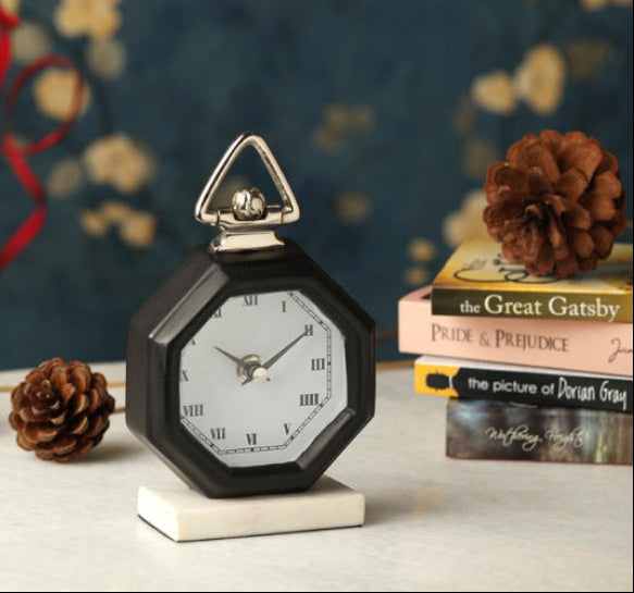 Decorative clock with Roman numerals on a surface with books and pinecones.