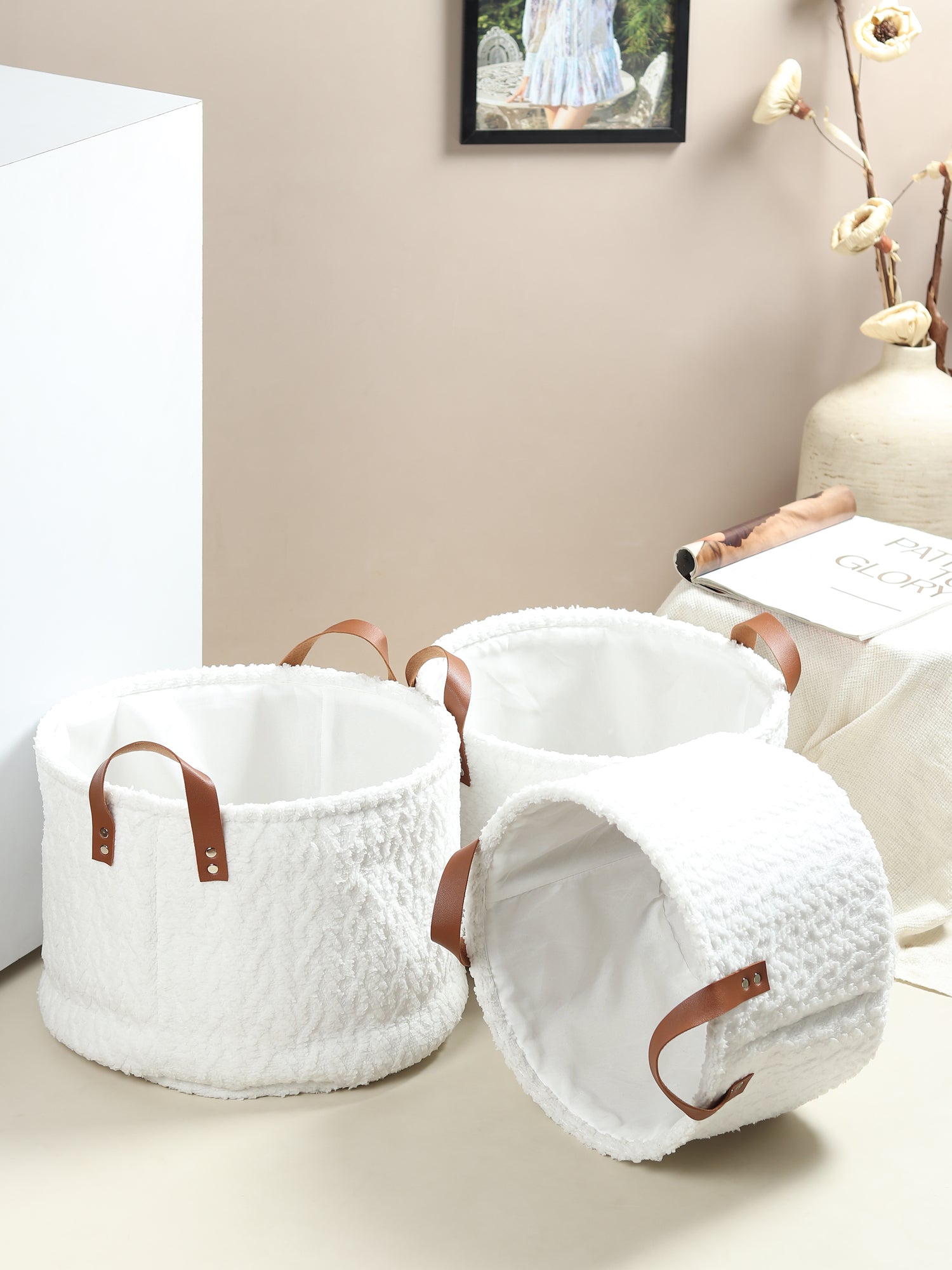Set of white textured storage baskets with brown handles on a light surface.