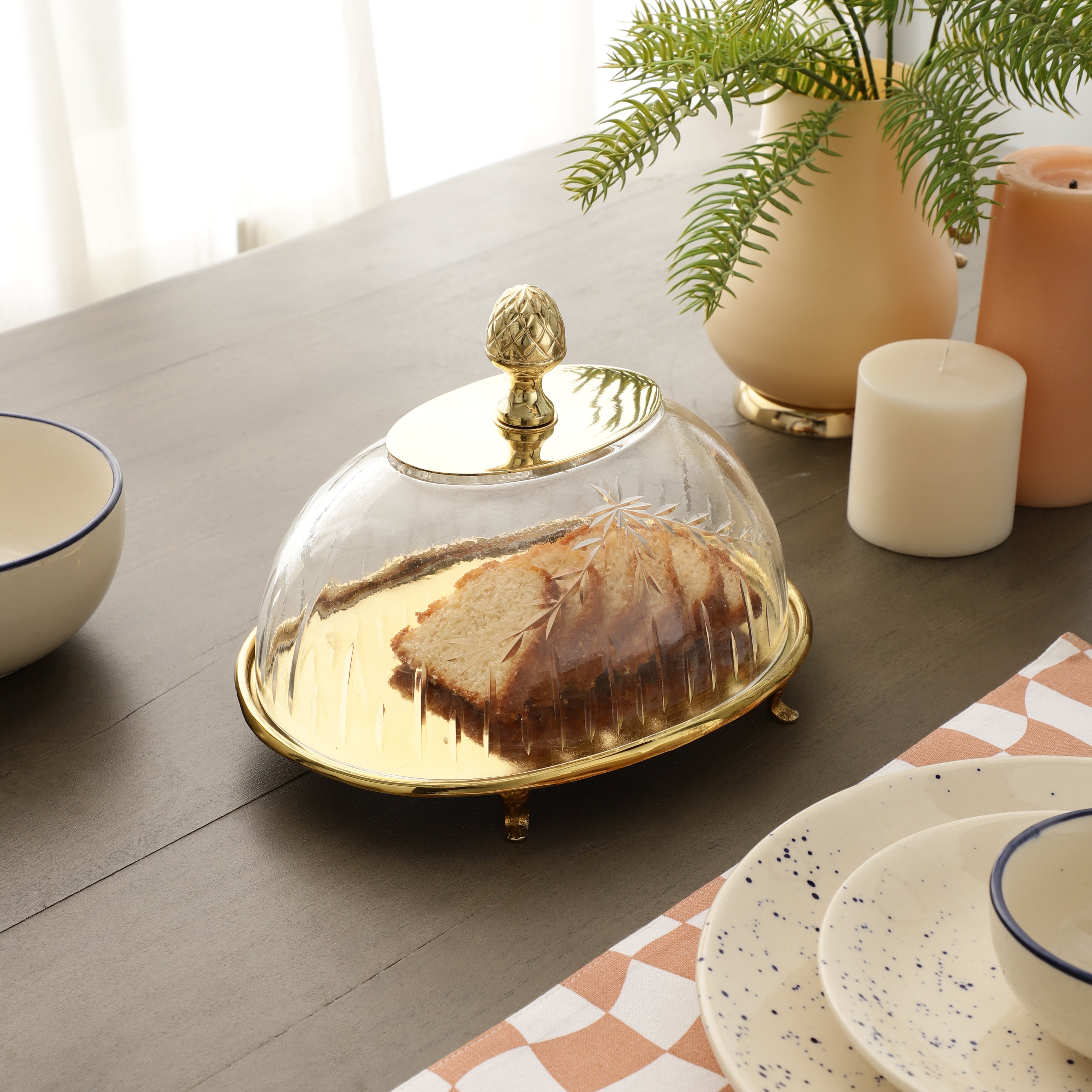 Glass cloche with gold rim on a table with bread inside, surrounded by decorative items.