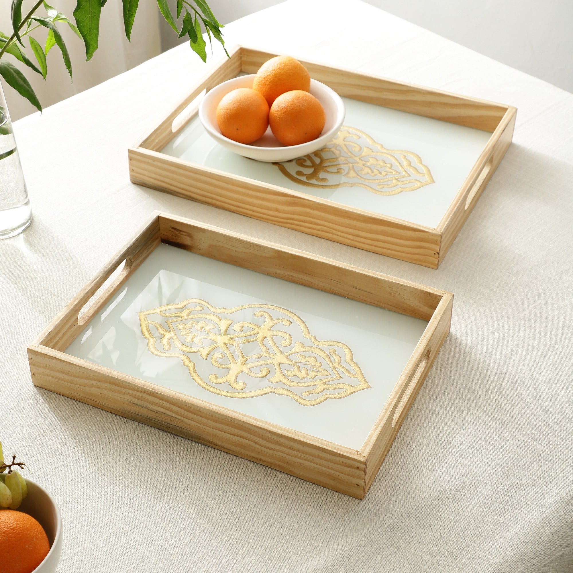 Two wooden trays with decorative gold patterns on a light surface.