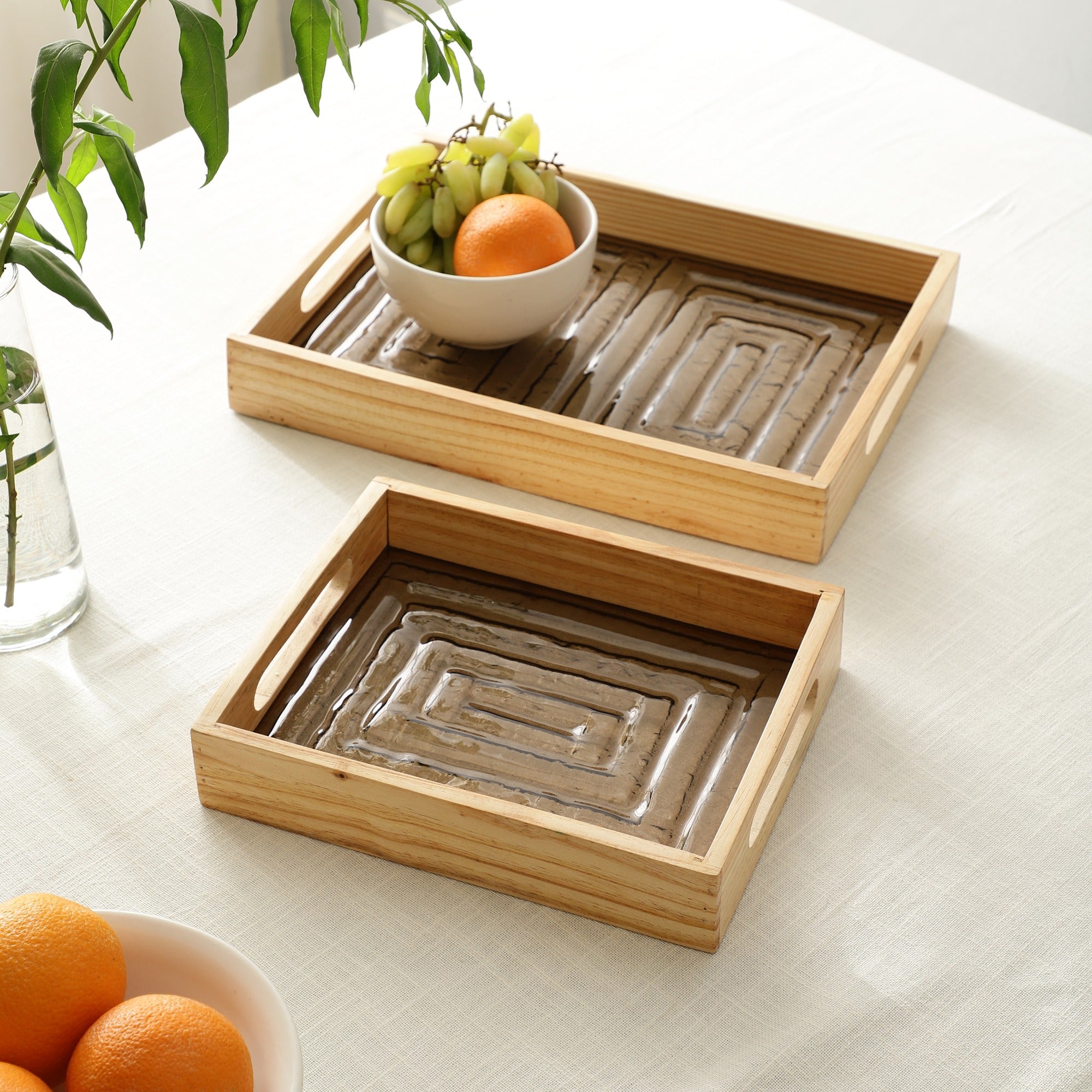Two wooden trays on a light surface with fruits and a plant.