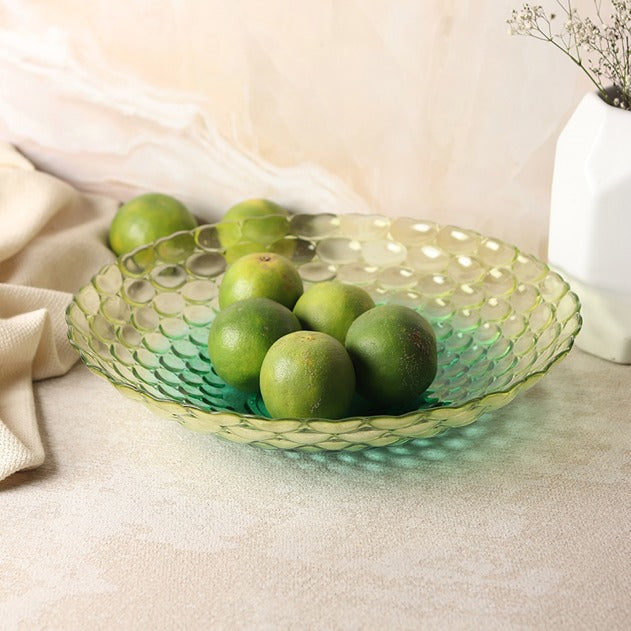 Green glass bowl with limes on a beige surface
