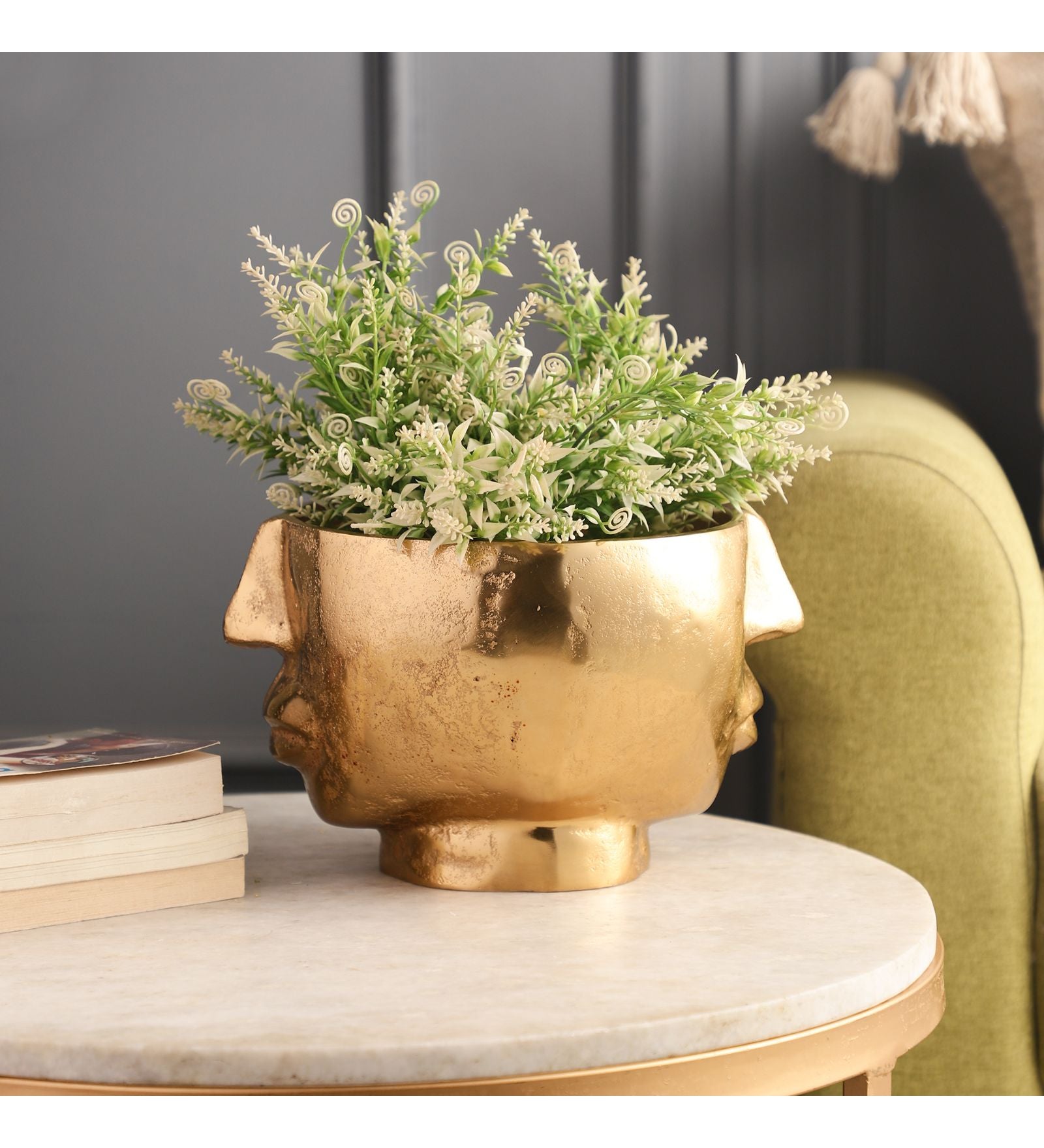 Gold decorative pot with a plant on a marble surface against a dark wall.