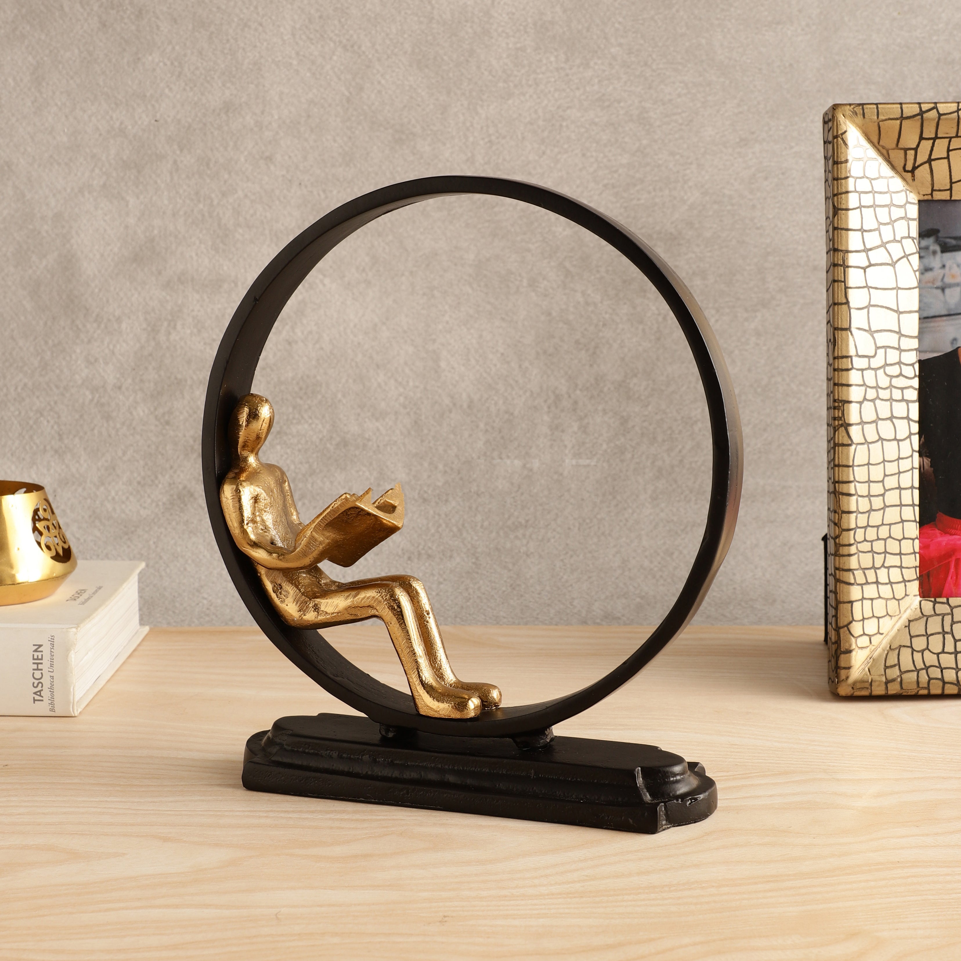 Decorative sculpture of a person reading a book inside a circular frame on a wooden surface.