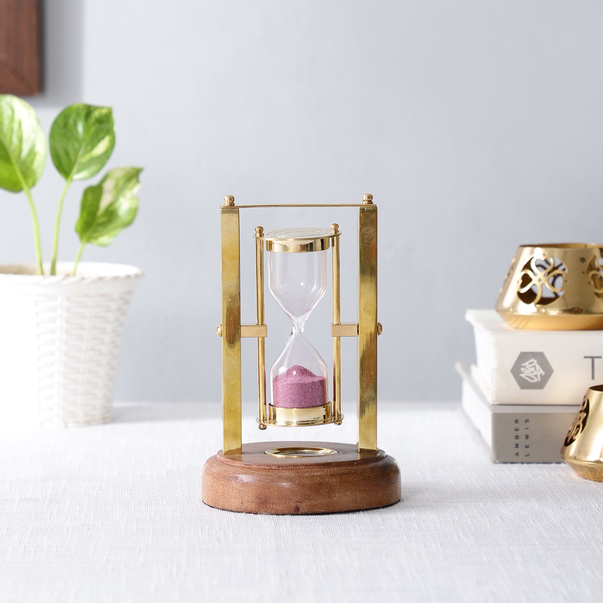 Decorative hourglass with gold frame and wooden base on a white surface.